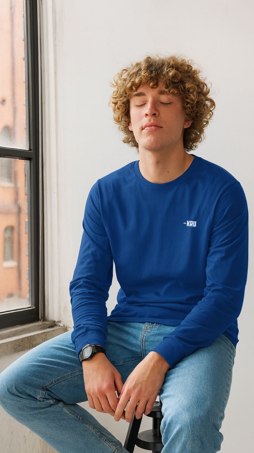 Person wearing a blue long-sleeve shirt sitting by a window