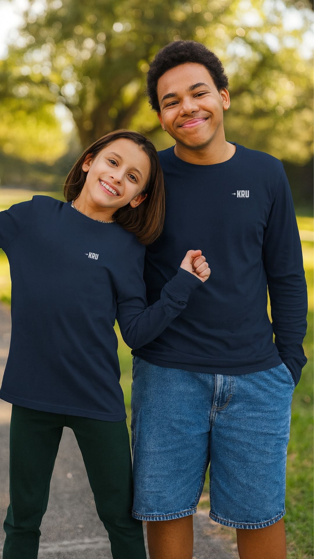 Two people wearing navy blue sweatshirts with a logo, standing outdoors in a park.