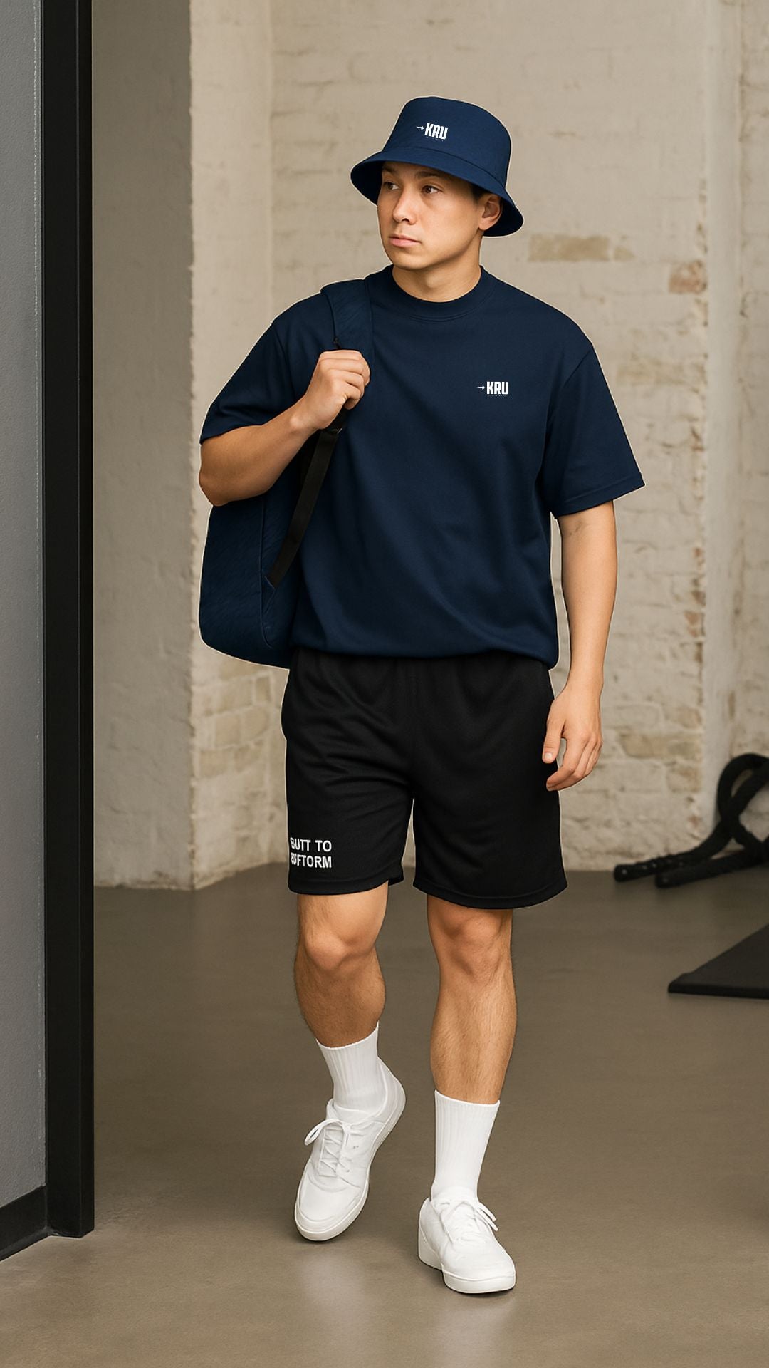 Man wearing navy t-shirt, black shorts, white sneakers, and navy bucket hat indoors.