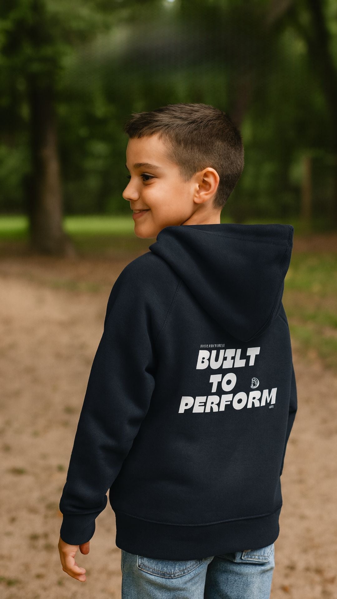 Child wearing a black hoodie with 'Built to Perform' text in a park setting