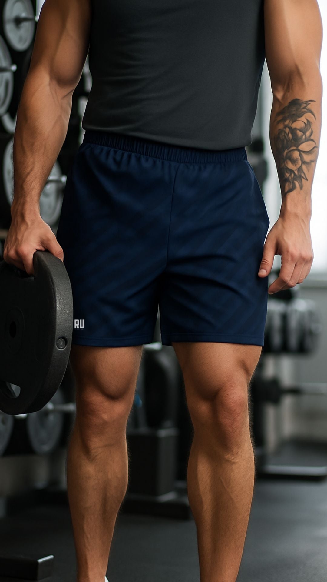 Person wearing navy shorts with a brand logo, holding a weight plate in a gym setting.