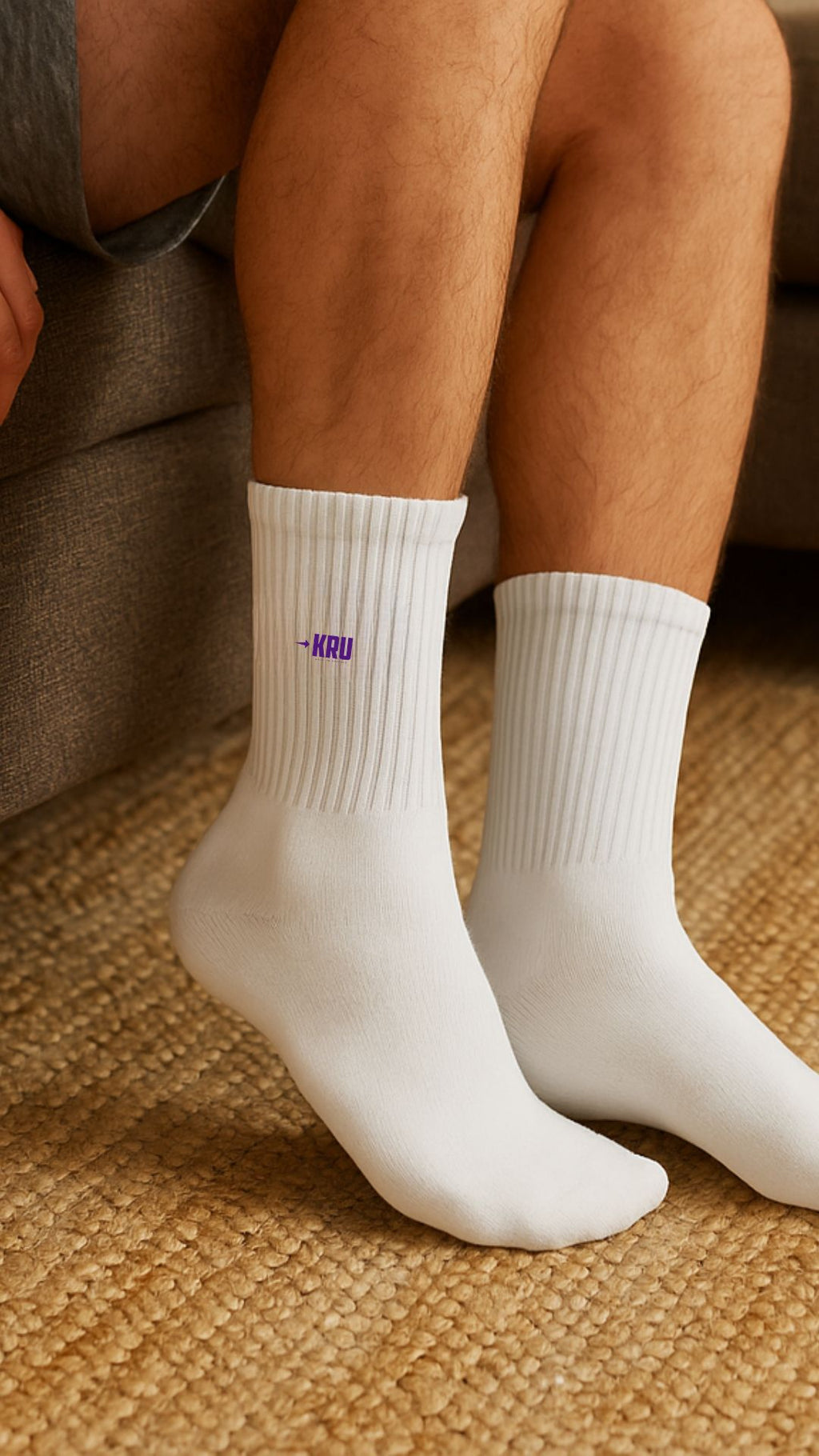 White socks with a logo on the foot worn by a person sitting on a textured surface.
